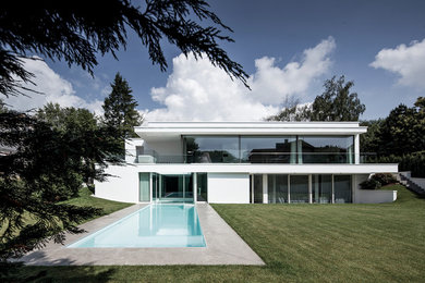 Cette photo montre une très grande façade de maison blanche moderne en stuc à un étage avec un toit plat.