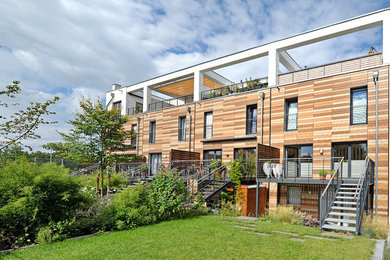 Imagen de fachada de casa pareada marrón contemporánea grande de tres plantas con tejado plano, revestimiento de madera y techo verde