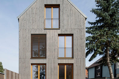 This is an example of a gey and medium sized contemporary house exterior in Berlin with three floors, a pitched roof and wood cladding.