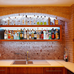 Diseño de bar en casa con barra de bar en L, mediterráneo, de tamaño medio, con armarios con paneles lisos, puertas de armario de madera en tonos medios, encimera de cemento, salpicadero marrón y salpicadero de azulejos de piedra