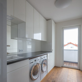 Idée de décoration pour une buanderie minimaliste avec des portes de placard blanches, un mur blanc et un sol en bois peint.