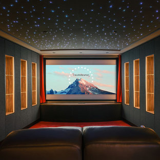 Imagen de cine en casa actual, grande, con paredes grises, moqueta, pantalla de proyección y suelo rojo