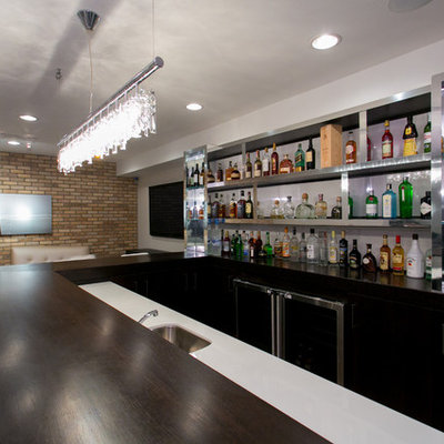 Example of a large trendy u-shaped dark wood floor seated home bar design in New York with glass countertops, white backsplash and black cabinets