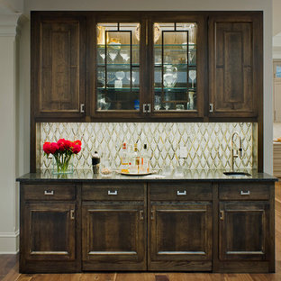 Foto di un grande angolo bar con lavandino tradizionale con pavimento in legno massello medio, lavello da incasso, ante con bugna sagomata, ante in legno bruno, top in laminato, paraspruzzi multicolore, pavimento marrone e top nero