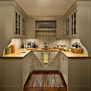 Imagen de bar en casa en U, de estilo de casa de campo, con puertas de armario grises, encimera de madera, salpicadero verde, suelo de madera en tonos medios, fregadero bajoencimera, armarios tipo vitrina, suelo marrón y encimeras marrones