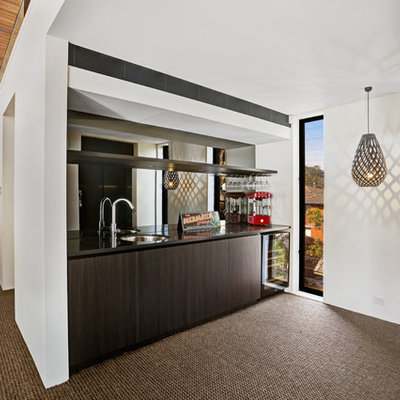 Small trendy carpeted home bar photo in Central Coast with an undermount sink, flat-panel cabinets, dark wood cabinets, solid surface countertops, black backsplash, mirror backsplash and black countertops