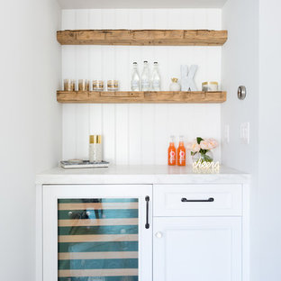 Cette photo montre un petit bar de salon avec évier linéaire chic avec aucun évier ou lavabo, des portes de placard blanches, un plan de travail en marbre, une crédence blanche, une crédence en bois, un sol en bois clair, un plan de travail blanc et un placard avec porte à panneau encastré.
