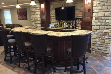 Example of a large arts and crafts single-wall ceramic tile and multicolored floor seated home bar design in St Louis with an undermount sink, raised-panel cabinets, granite countertops, beige backsplash, stone tile backsplash and medium tone wood cabinets