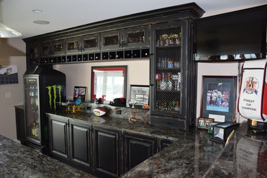 Home bar - 1950s home bar idea in Detroit with raised-panel cabinets, distressed cabinets, granite countertops, stone slab backsplash and an undermount sink