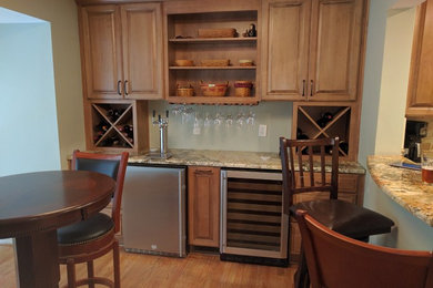 Design ideas for a small traditional single-wall wet bar in Raleigh with granite worktops, light hardwood flooring, raised-panel cabinets and medium wood cabinets.