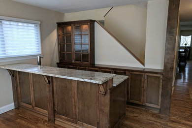 Example of a classic dark wood floor and brown floor home bar design in New York with shaker cabinets, dark wood cabinets and granite countertops