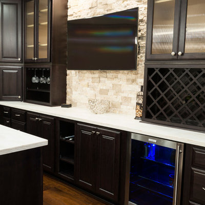Inspiration for a mid-sized contemporary galley dark wood floor seated home bar remodel in Indianapolis with dark wood cabinets, solid surface countertops, beige backsplash, stone tile backsplash, an undermount sink and raised-panel cabinets