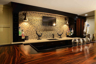 Example of a mid-sized transitional galley dark wood floor and brown floor seated home bar design in New York with an undermount sink, flat-panel cabinets, black cabinets, limestone countertops, beige backsplash and stone tile backsplash