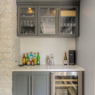 Diseño de bar en casa lineal, tradicional renovado, pequeño, con armarios estilo shaker, puertas de armario grises, suelo de madera en tonos medios y encimeras blancas