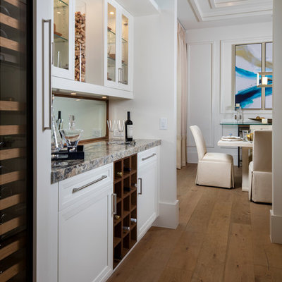 Example of a beach style single-wall medium tone wood floor home bar design in Miami with no sink, glass-front cabinets, white cabinets, mirror backsplash and multicolored countertops