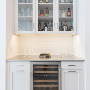 Inspiration for a farmhouse single-wall home bar remodel in New York with shaker cabinets, white cabinets, stainless steel countertops, white backsplash, glass tile backsplash and gray countertops
