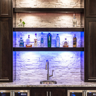Cette photo montre un très grand bar de salon avec évier linéaire tendance avec un évier encastré, un placard à porte shaker, des portes de placard en bois sombre, un plan de travail en granite, une crédence blanche, une crédence en carrelage de pierre et un sol en bois clair.
