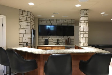 Trendy u-shaped carpeted seated home bar photo in Omaha with flat-panel cabinets, medium tone wood cabinets, granite countertops, an undermount sink and beige backsplash