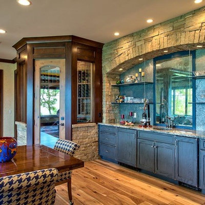 Example of a mid-sized mountain style single-wall light wood floor wet bar design in Other with an undermount sink, recessed-panel cabinets, distressed cabinets, granite countertops, gray backsplash and stone slab backsplash