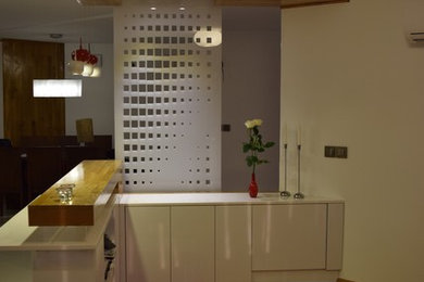 Diseño de bar en casa en L moderno pequeño sin pila con armarios con paneles lisos, puertas de armario blancas, encimera de vidrio, salpicadero blanco, salpicadero de vidrio templado y suelo de madera clara