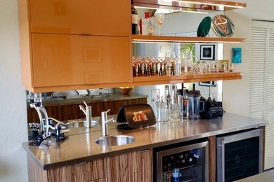 Modelo de bar en casa con fregadero lineal vintage de tamaño medio con fregadero integrado, armarios con paneles lisos, puertas de armario naranjas, encimera de acero inoxidable y salpicadero con efecto espejo