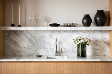 Immagine di un piccolo angolo bar moderno con lavello sottopiano, ante in legno chiaro, top in marmo, paraspruzzi bianco, paraspruzzi in lastra di pietra e top bianco