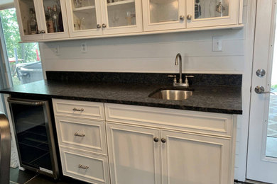 This is an example of a small contemporary galley wet bar in Indianapolis with recessed-panel cabinets, white cabinets, granite worktops, ceramic flooring, black floors and black worktops.