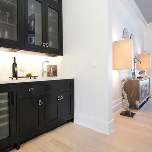 Immagine di un angolo bar senza lavandino design di medie dimensioni con ante con bugna sagomata, ante nere, top in marmo, paraspruzzi bianco, parquet chiaro, pavimento beige e top bianco