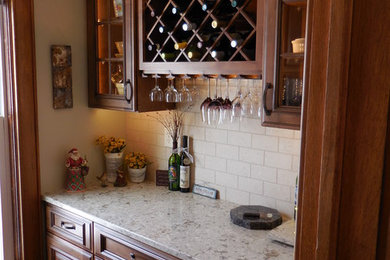 Example of a mid-sized classic single-wall medium tone wood floor and brown floor home bar design in Chicago with no sink, raised-panel cabinets, medium tone wood cabinets, granite countertops, white backsplash and subway tile backsplash
