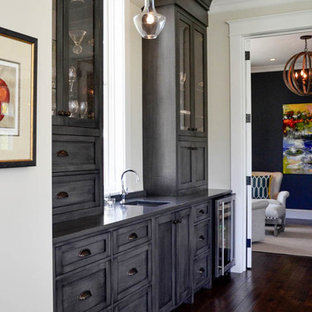 Foto de bar en casa con fregadero lineal, clásico renovado, con fregadero bajoencimera, armarios con paneles lisos, puertas de armario grises, suelo de madera oscura y suelo marrón
