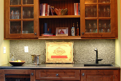 This is an example of a small rustic single-wall wet bar in Portland Maine with a submerged sink, glass-front cabinets, medium wood cabinets, granite worktops, grey splashback, stone tiled splashback and medium hardwood flooring.