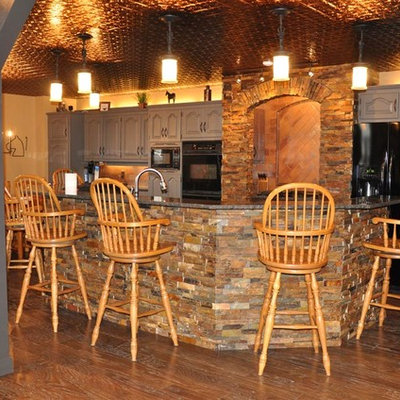 Mid-sized mountain style u-shaped medium tone wood floor and brown floor wet bar photo in Other with raised-panel cabinets, gray cabinets, granite countertops and beige backsplash
