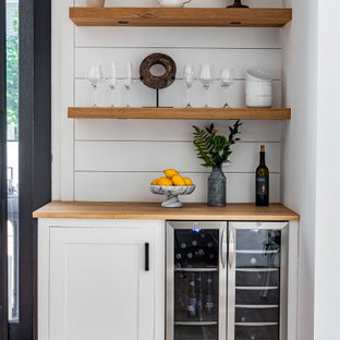 Foto de bar en casa lineal, clásico renovado, pequeño, sin pila, con armarios estilo shaker, puertas de armario blancas, encimera de madera, salpicadero blanco, salpicadero de madera, suelo de madera clara, suelo beige y encimeras beige
