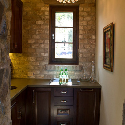 Example of a large mountain style single-wall medium tone wood floor wet bar design in San Francisco with an undermount sink, raised-panel cabinets, dark wood cabinets, solid surface countertops, brown backsplash and brick backsplash