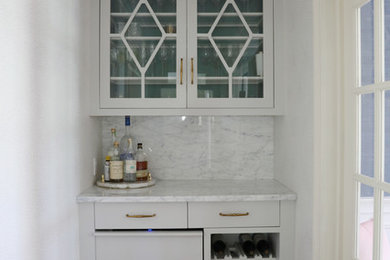 Example of a small transitional single-wall dark wood floor and brown floor dry bar design in New York with no sink, glass-front cabinets, gray cabinets, marble countertops, gray backsplash, marble backsplash and gray countertops