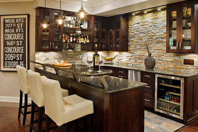 Example of a large transitional u-shaped dark wood floor seated home bar design in New York with glass-front cabinets, dark wood cabinets, multicolored backsplash, stone tile backsplash, gray countertops and granite countertops