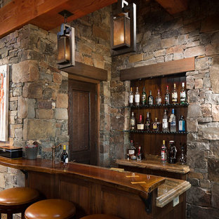 Foto de bar en casa con barra de bar de galera, rústico, de tamaño medio, con suelo de madera oscura, armarios estilo shaker, puertas de armario de madera en tonos medios, encimera de madera, salpicadero multicolor, salpicadero de azulejos de piedra y suelo marrón