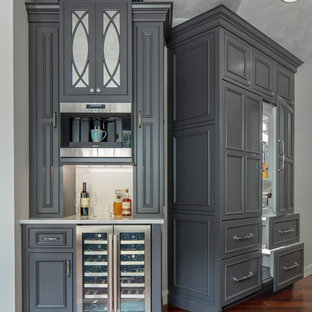 Ejemplo de bar en casa lineal, tradicional, pequeño, sin pila, con puertas de armario grises, encimera de cuarzo compacto, encimeras blancas, salpicadero blanco, armarios con rebordes decorativos y suelo de madera oscura