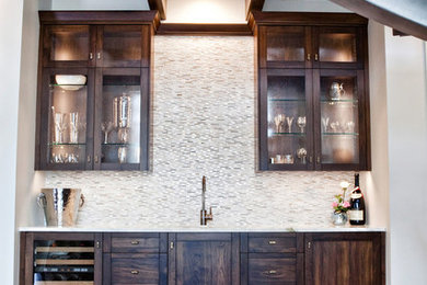 Inspiration for a mid-sized transitional single-wall medium tone wood floor wet bar remodel in Boise with a drop-in sink, glass-front cabinets, dark wood cabinets, granite countertops, white backsplash and stone tile backsplash