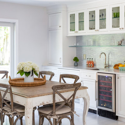 Example of a beach style single-wall light wood floor and beige floor wet bar design in New York with an undermount sink, glass-front cabinets, white cabinets, gray backsplash and gray countertops