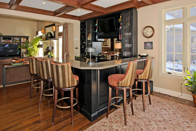 Example of a mid-sized classic single-wall medium tone wood floor seated home bar design in Cleveland with black cabinets, raised-panel cabinets, mirror backsplash, granite countertops and a drop-in sink
