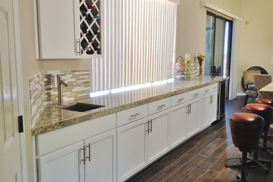 Photo of a medium sized contemporary single-wall wet bar in Phoenix with a submerged sink, shaker cabinets, white cabinets, granite worktops, beige splashback, glass tiled splashback, laminate floors and brown floors.