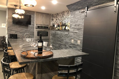 Mid-sized trendy l-shaped seated home bar photo in New York with soapstone countertops, gray backsplash, slate backsplash and black countertops