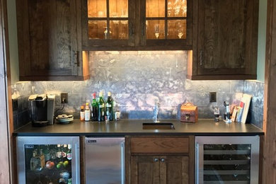This is an example of a medium sized rustic single-wall wet bar in Other with a submerged sink, shaker cabinets, dark wood cabinets, composite countertops, grey splashback, metal splashback, light hardwood flooring and beige floors.