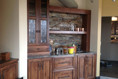 Example of a small mountain style single-wall carpeted wet bar design in Milwaukee with an undermount sink, recessed-panel cabinets, dark wood cabinets, granite countertops and slate backsplash