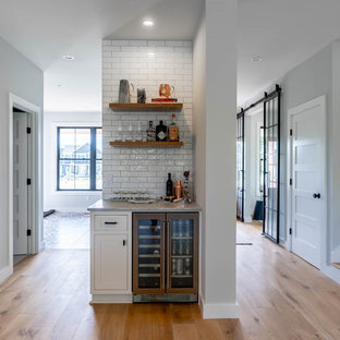 Diseño de bar en casa lineal, campestre, pequeño, sin pila, con armarios estilo shaker, puertas de armario blancas, salpicadero blanco, salpicadero de azulejos tipo metro, suelo de madera clara, suelo beige y encimeras grises