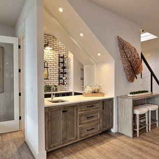 Ejemplo de bar en casa con fregadero en U, de estilo de casa de campo, grande, con fregadero bajoencimera, armarios estilo shaker, puertas de armario con efecto envejecido, encimera de cuarzo compacto, salpicadero blanco, salpicadero de ladrillos, suelo de madera en tonos medios, suelo marrón y encimeras blancas