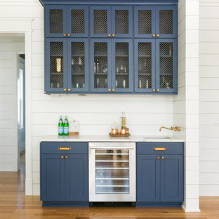 Foto di un angolo bar con lavandino country di medie dimensioni con ante blu, top bianco, lavello sottopiano, ante con riquadro incassato, top in marmo, paraspruzzi bianco, paraspruzzi in legno, pavimento in legno massello medio e pavimento marrone