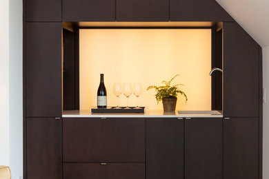 Example of a small minimalist single-wall light wood floor and brown floor wet bar design in San Francisco with an undermount sink, flat-panel cabinets, brown cabinets, quartz countertops, white backsplash, glass sheet backsplash and white countertops