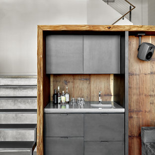 Imagen de bar en casa con fregadero lineal, moderno, de tamaño medio, con suelo de cemento, suelo gris, fregadero integrado, armarios con paneles lisos, puertas de armario grises, encimera de acero inoxidable, salpicadero marrón y salpicadero de madera